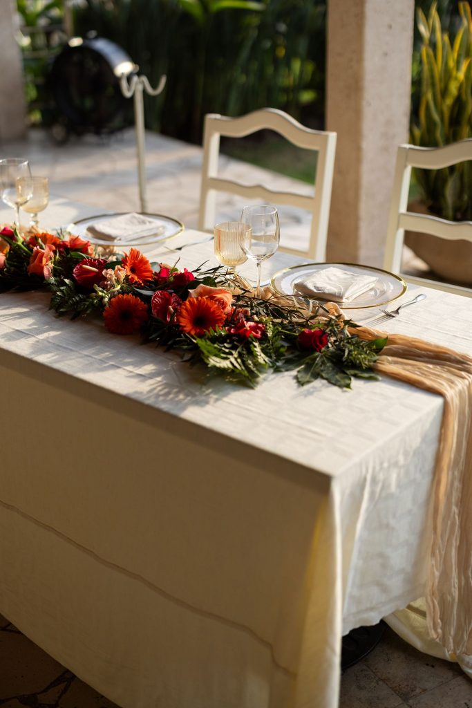 Wedding table with red flower garland and glassware at golden hour at Oscar's Puerto Vallarta
